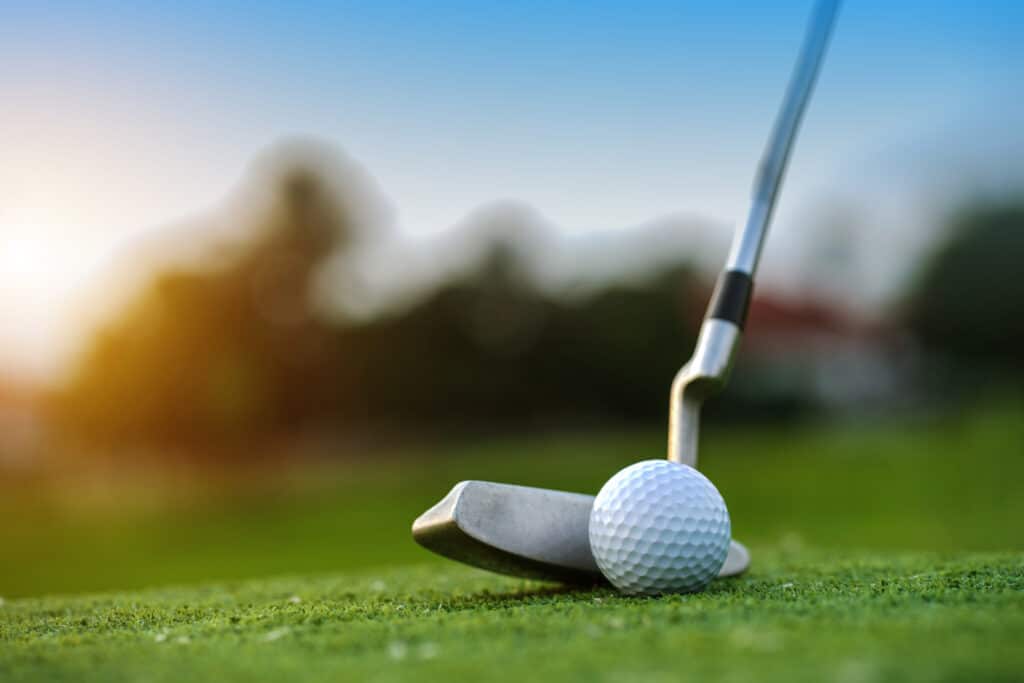 Golf clubs and golf balls on a green lawn in a beautiful golf course with morning sunshine.