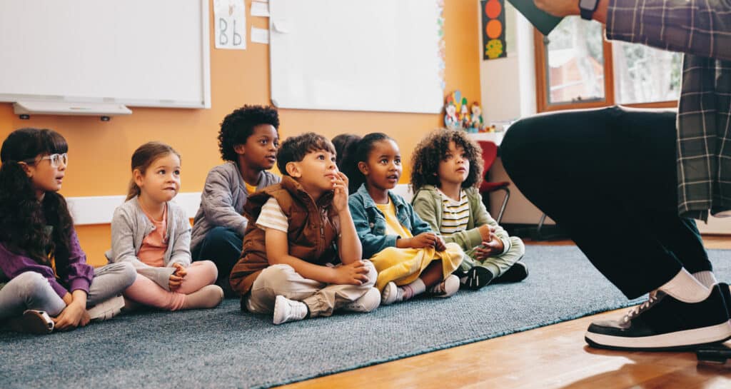 Elementary school students sit and listen to a story from their teacher