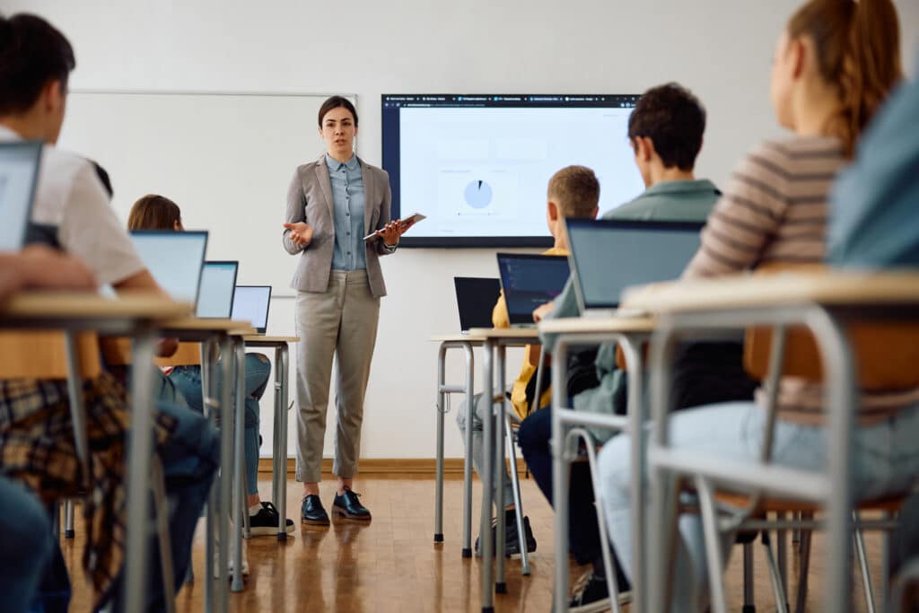 Female professor talking to her students during IT class at high school.